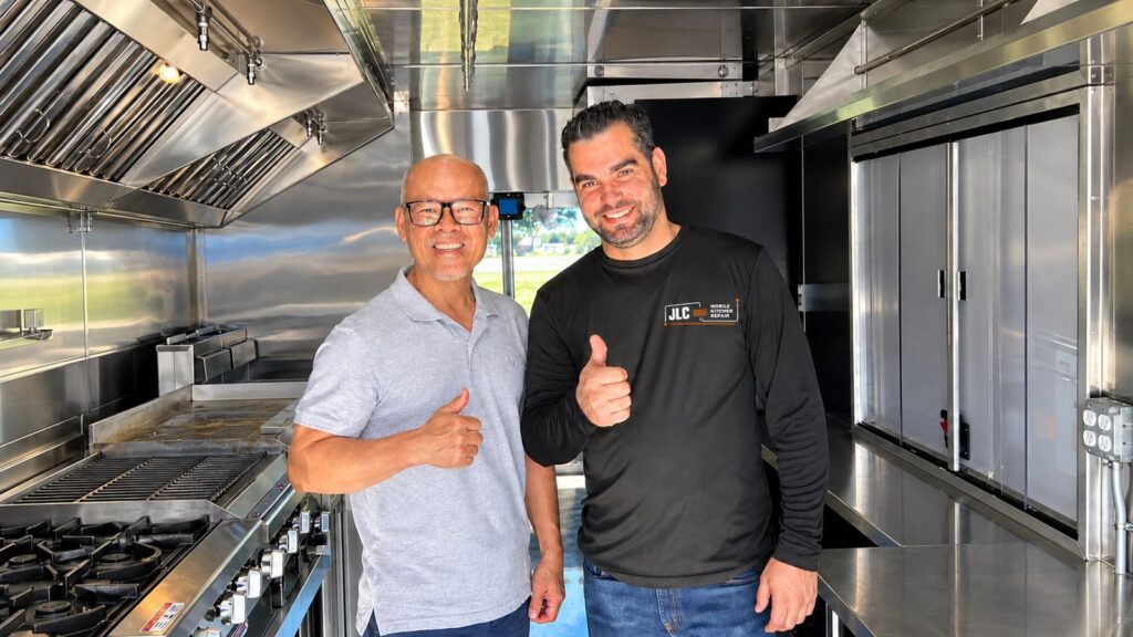 Commercial Kitchen Hood Installation: What to Prepare Before Requesting a Quote Two men standing beside a commercial cooking line beneath a stainless steel exhaust hood.